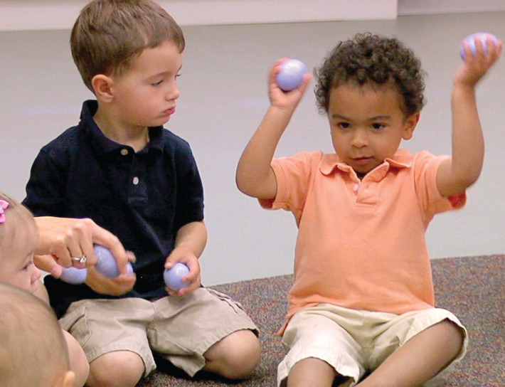 Two children sitting on the floor playing with balls.