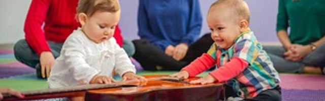 Two babies playing with a guitar while sitting on the floor.